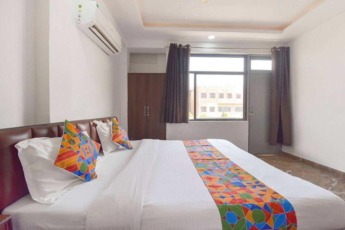 Habitación de hotel con cama, ventana con cortinas, puerta y equipo de aire acondicionado en la pared.