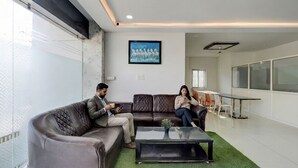 A modern office space with leather couches, a glass partition, and a large window. - Fabhotel Pgr Guest Inn (Hyderabad)