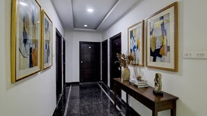 A hallway with framed abstract art, a dark door, and a console table with decorative items. - Fabhotel Pgr Guest Inn (Hyderabad)