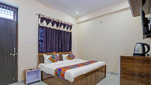 A bedroom with a wooden bed, a nightstand, a dresser, a kettle, and a window with curtains. - Fabhotel Dwarika Inn (Varanasi)