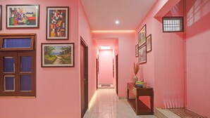 A hallway with pink walls, framed artwork, and a wooden console table with decorative items. - Fabhotel Dwarika Inn (Varanasi)