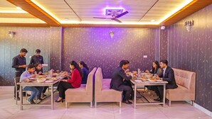 A dining area with tables and sofas, a ceiling fan, and patterned wallpaper. - Fabhotel Dwarika Inn (Varanasi)