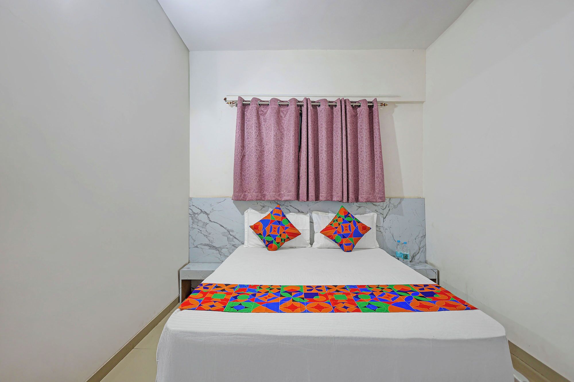 A hotel room with a bed, a marble headboard, a pink curtain, and two decorative pillows.