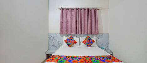 A hotel room with a bed, a marble headboard, a pink curtain, and two decorative pillows.