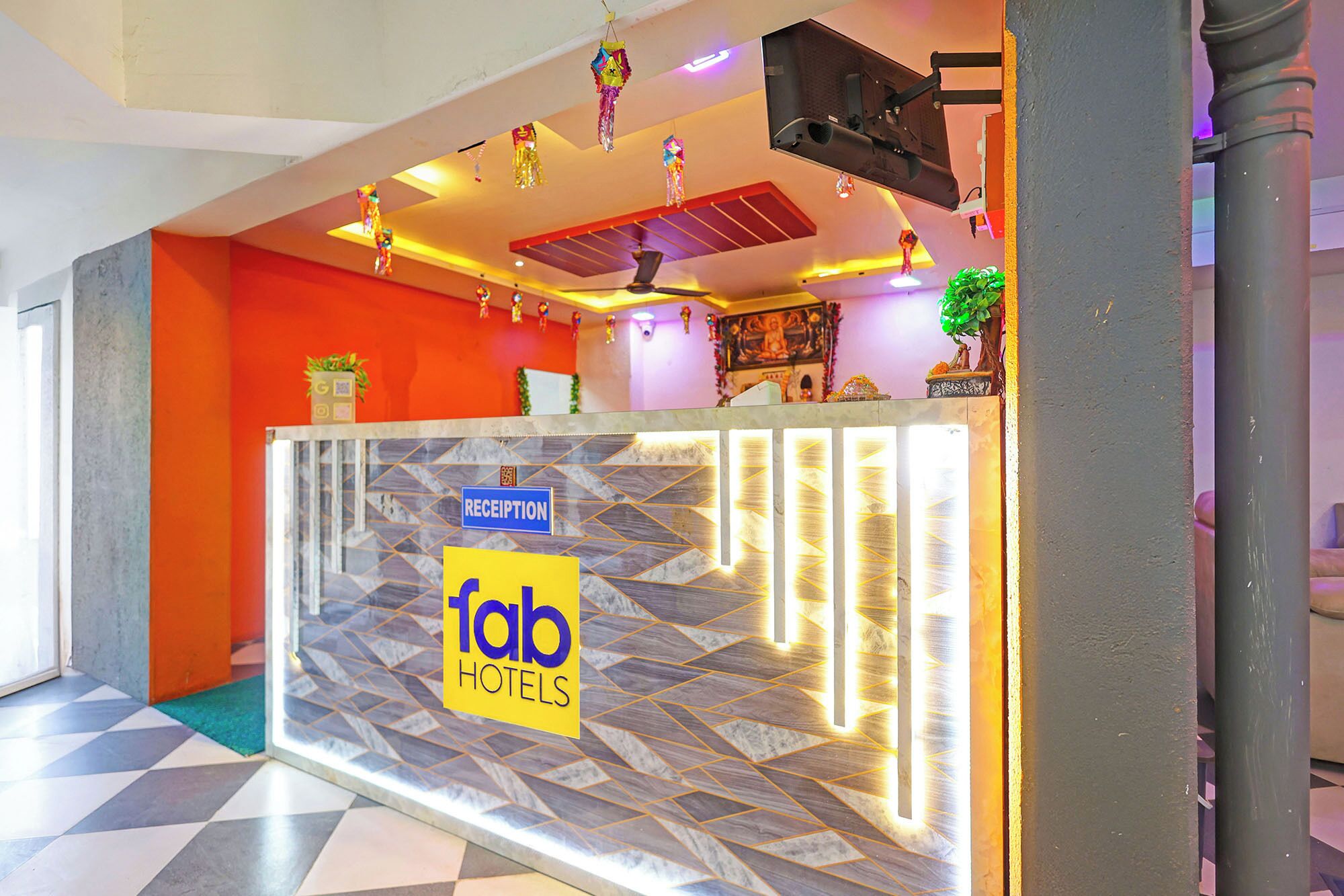 Ein Empfangsschalter mit einem 'Reception'-Schild und dem 'Tab Hotels'-Logo, einem Deckenventilator und dekorativen Hängeornamenten.