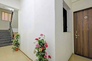 A hallway with a staircase, a wooden door with a number, and a floral arrangement.