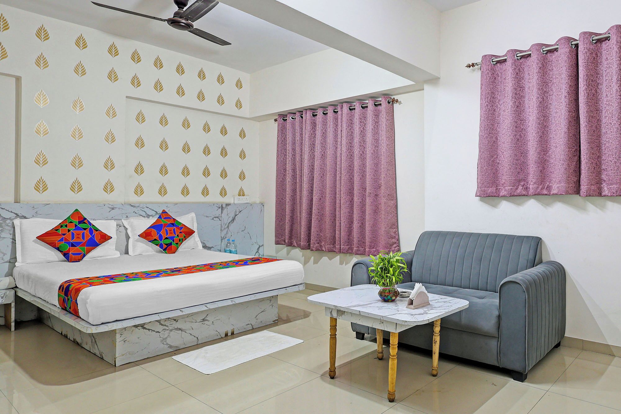 A bedroom with a bed, a sofa, a small table with a plant, and a window with curtains.