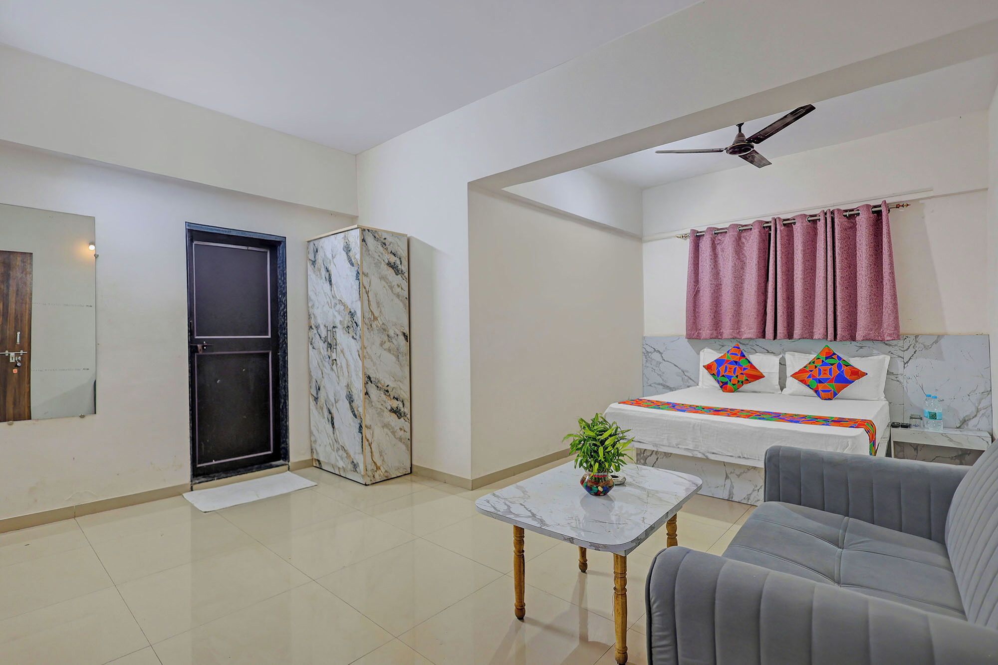 Un salon moderne avec un canapé, une table basse, un lit agrémenté de coussins colorés, un ventilateur de plafond et un meuble en marbre.