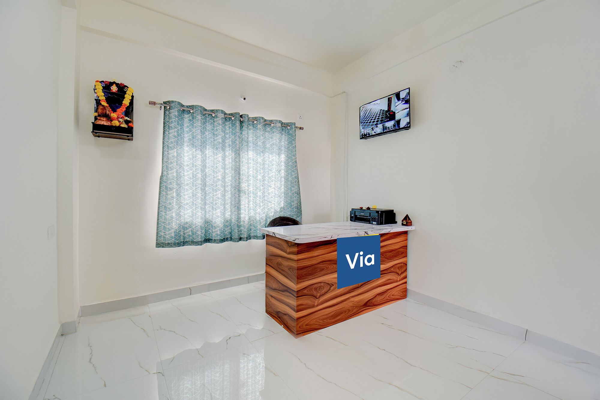 A reception desk with a 'Via' sign, a window with patterned curtains, and a wall-mounted picture.