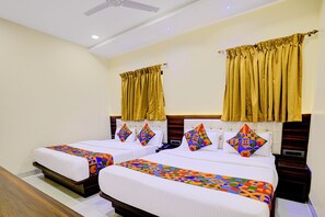 Habitación de hotel con dos camas, cada una con una colcha y almohadas a juego de estampado geométrico y colores vivos. La habitación tiene un cabecero de madera, un ventilador de techo y cortinas doradas.