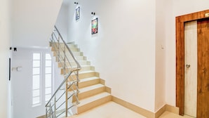 Una escalera con barandilla de metal, paredes blancas y una puerta de madera.