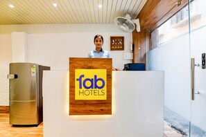 A reception desk with a logo for Fab Hotels, a wooden counter, a glass door, and a wall-mounted fan. - Fabhotel Adhiraj Inn (Kolkata)