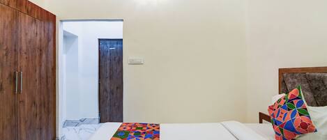 A bedroom with a bed, a wooden wardrobe, a door, and a light fixture.