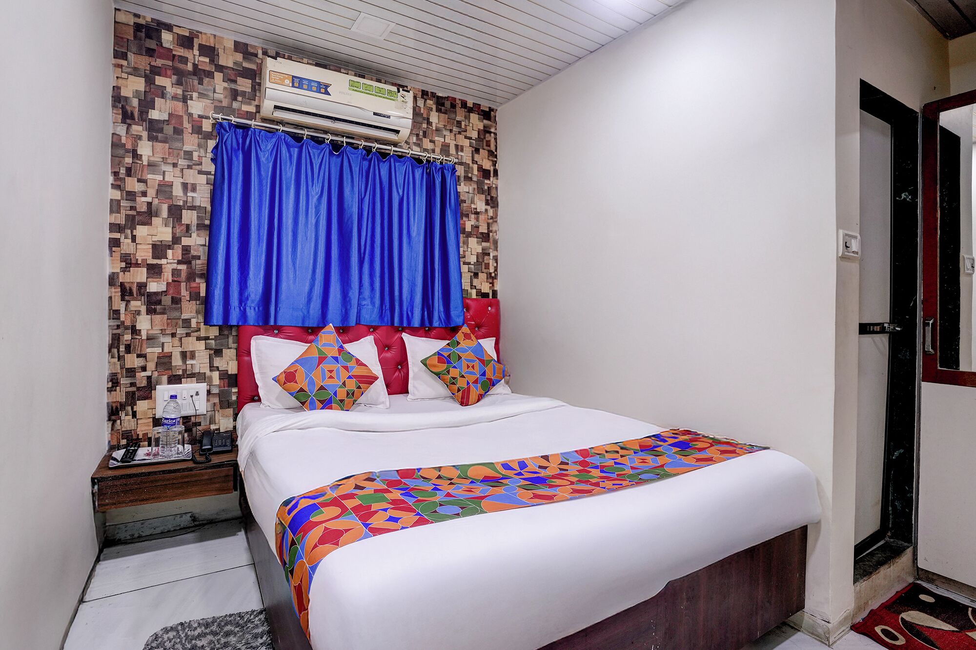 A hotel room with a bed, a red headboard, a blue curtain, and a wall with a mosaic pattern.