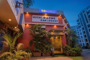 The facade of Hotel Saini Residency with a prominent sign, potted plants, and a modern building in the background.
