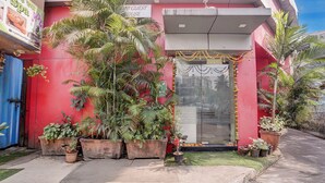 A building with a red facade, a glass door entrance, and multiple potted plants around the entrance. - Via Saini Residency (Mumbai)
