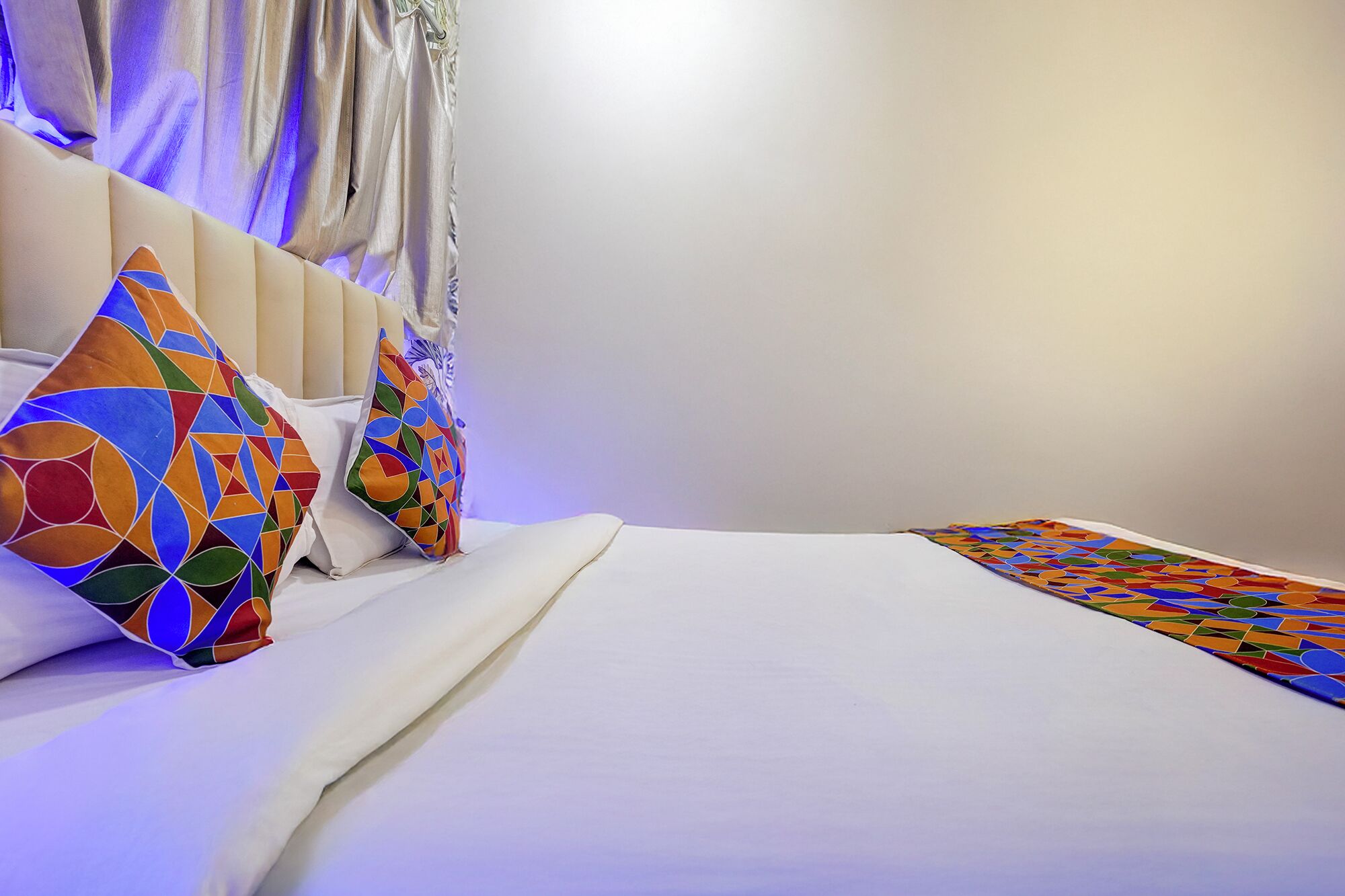 A neatly made bed with white linens and colorful geometric-patterned pillows.