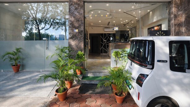 A modern building entrance with a reception desk, potted plants, and a white electric vehicle parked outside. - FabHotel Kamari Inn, Vijay Nagar (Indore)