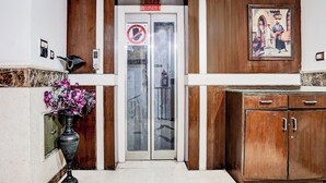 A hotel entrance with a glass door, a 'No Lift' sign, a fire extinguisher, a vase of flowers, and a wooden cabinet. - Fabhotel Shivdev International (New Delhi)