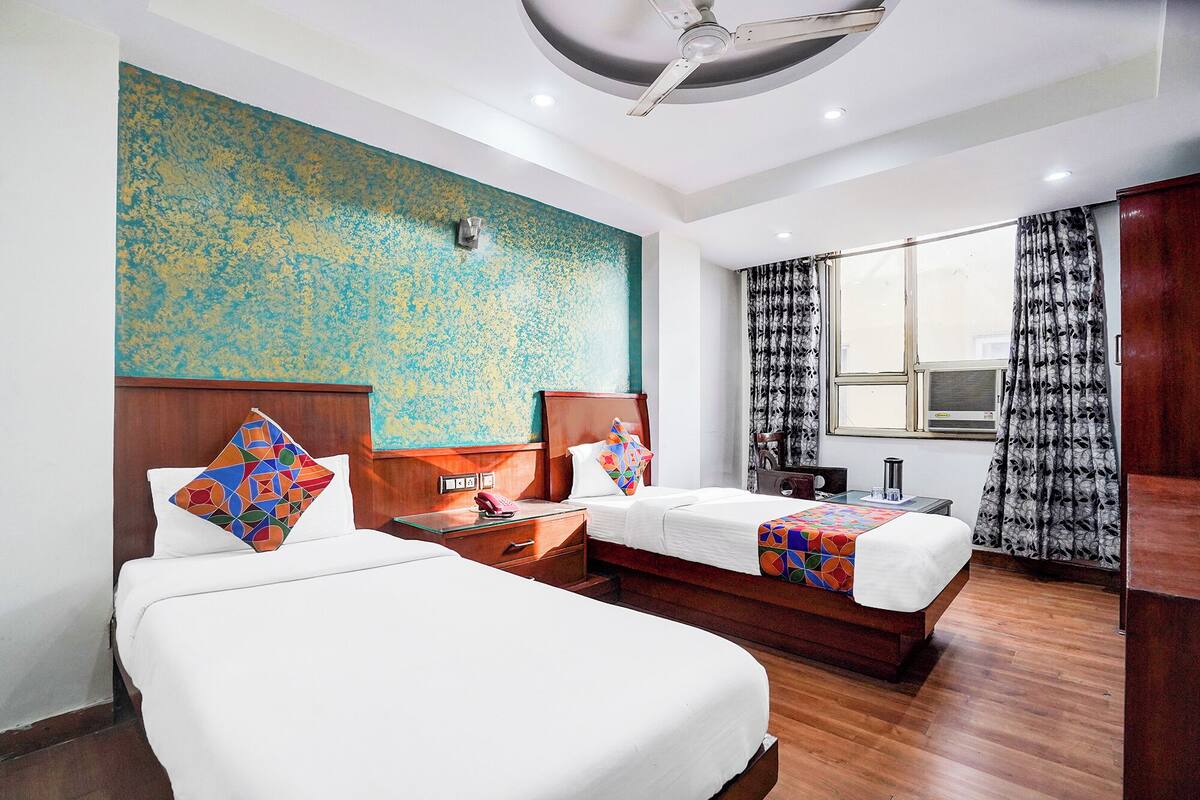 Habitación de hotel con dos camas, un ventanal con cortinas, un ventilador de techo y una pared con un mural texturizado.