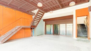 Ein großzügiger Innenraum mit einer Holztreppe, einer großen Schiebeglastür und einer hohen Decke mit freiliegenden Balken.