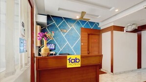 Ein Hotelrezeptionstresen mit blauer Wandverkleidung mit Muster, einer Holztresen und einem Schild mit der Aufschrift 'Tab Hotels'.