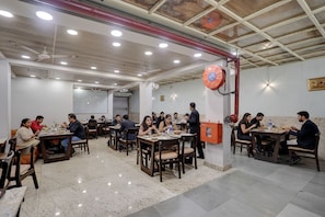 A restaurant with multiple tables and chairs, ceiling fans, and recessed lighting. - Fabhotel Aliza (Kolkata)