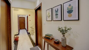 A hallway with a wooden door, a potted plant, and a small table with books and a vase. - Fabhotel Aliza (Kolkata)