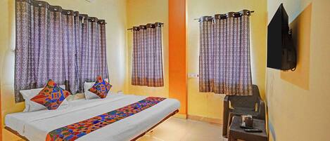 Habitación de hotel con cama, dos almohadas, televisor montado en la pared y cortinas.