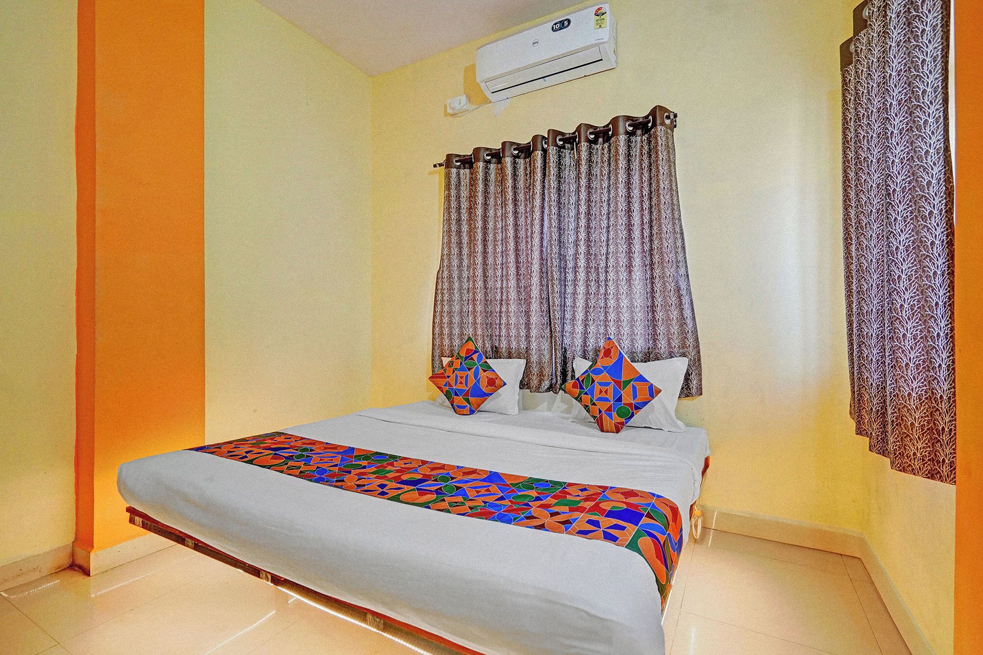 A bedroom with a bed, two pillows, a patterned curtain, and an air conditioning unit.