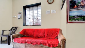 A room with a wooden sofa covered in a red blanket, a window with a view, a wall clock, and a poster on the wall. - Via Seven Hills Inn (Mawal)