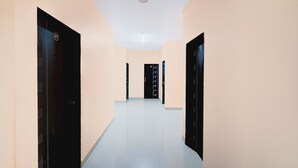 A hallway with cream-colored walls and black doors, leading to a room with a white ceiling and a visible light fixture. - Via Seven Hills Inn (Mawal)