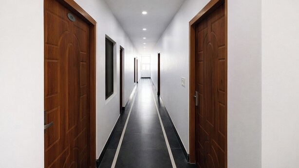 Un long couloir étroit, avec des portes en bois de chaque côté, des murs blancs et un sol recouvert de carreaux noirs.