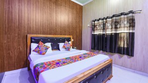Une chambre à coucher avec une tête de lit en bois, une couvre-lit à motifs et une fenêtre agrémentée de rideaux décoratifs.