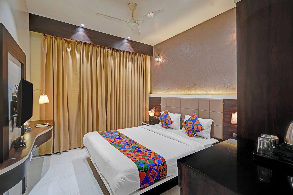 A hotel room with a bed, bedside lamps, a desk, a television, and a ceiling fan.