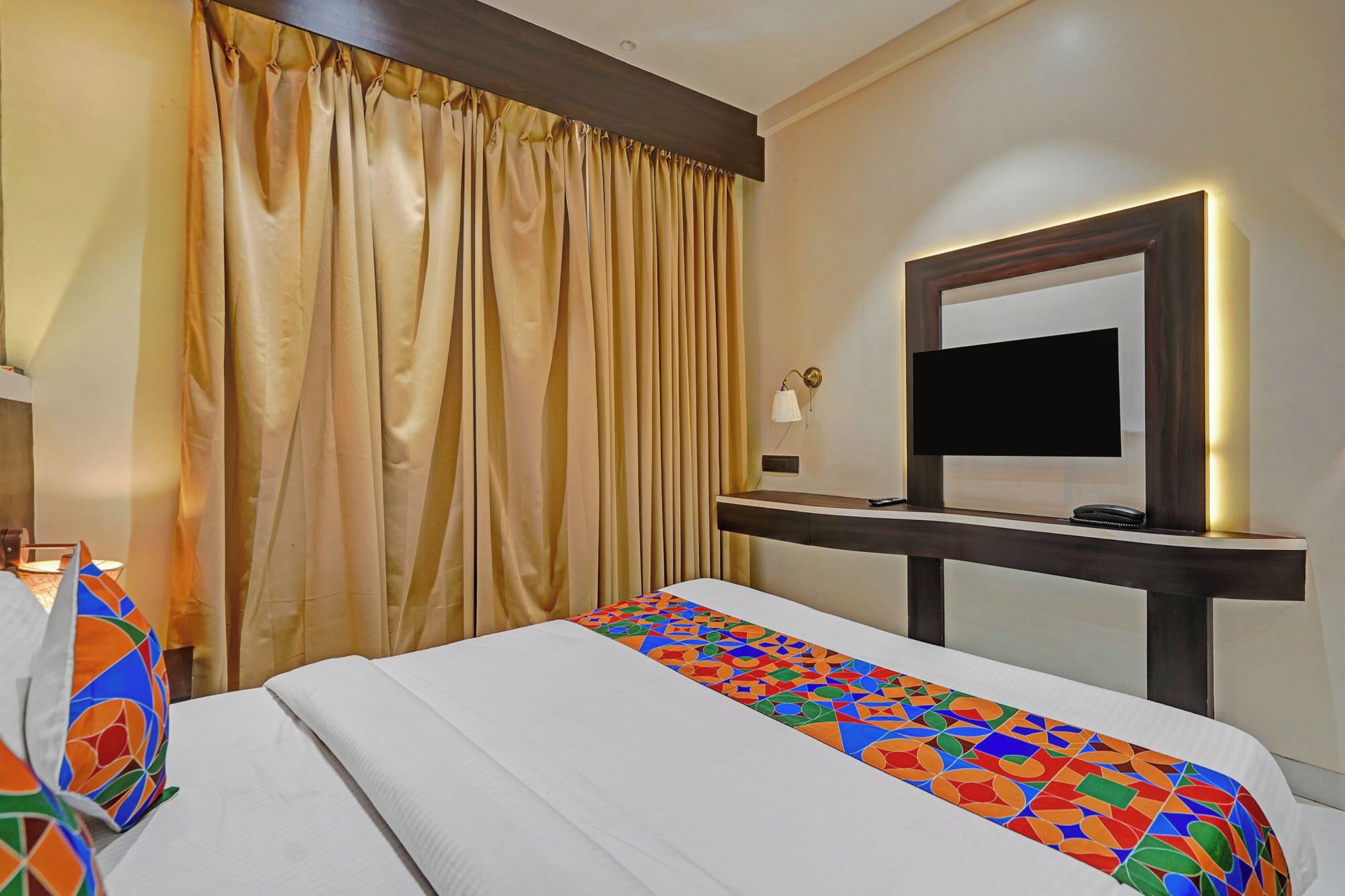 Una habitación de hotel con cama, televisión, escritorio y un ventanal con cortinas.