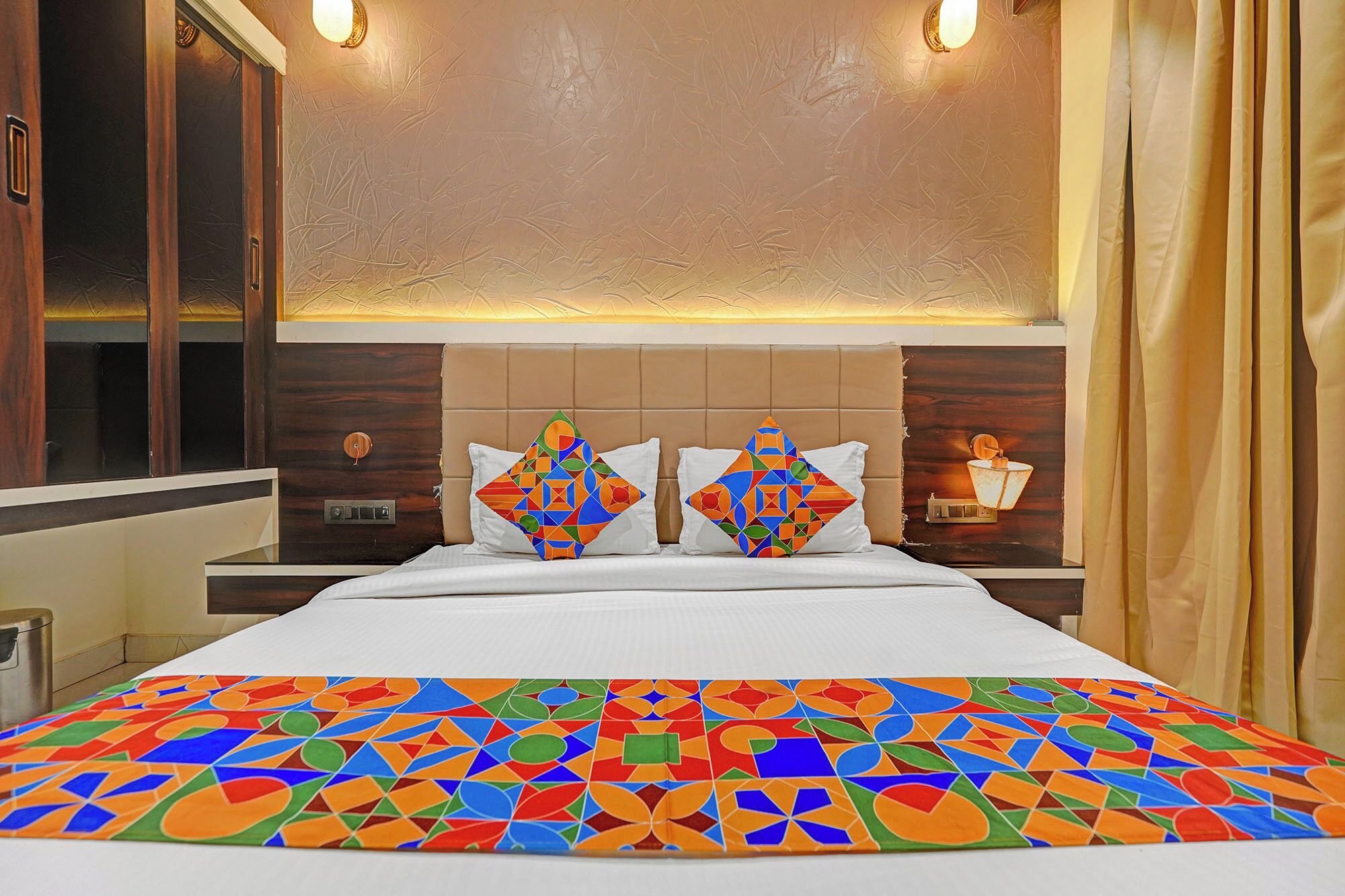 Habitación de hotel con cama, dos mesitas de noche, cabecera y ventana con cortinas.