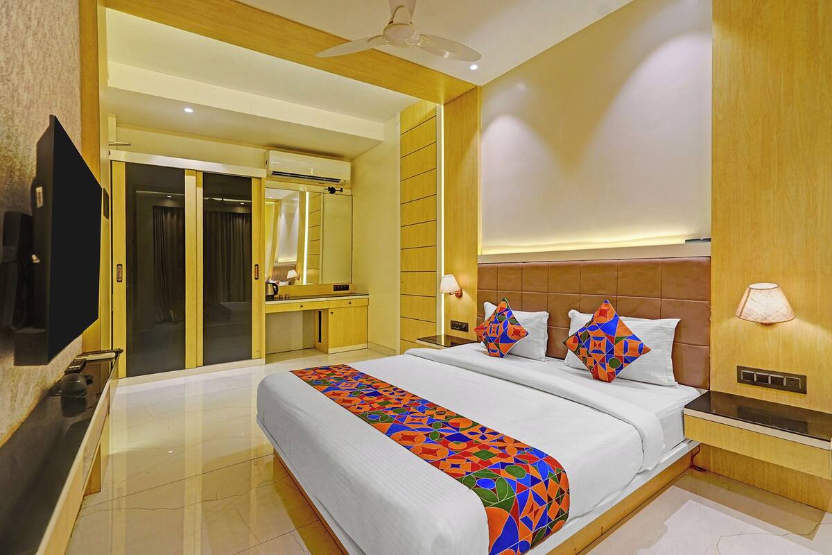 A modern hotel room with a large bed, a desk, a mirror, and a television.