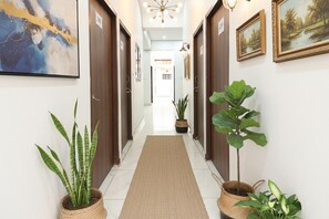 Un couloir agrémenté d’un tapis central, de plantes en pot et de tableaux encadrés accrochés aux murs.