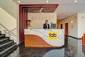 A hotel reception desk with a marble design, a ceiling fan, and a staircase leading to the upper floor.