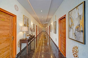 A hotel hallway with wooden doors, numbered room signs, framed artwork, and a marble floor.