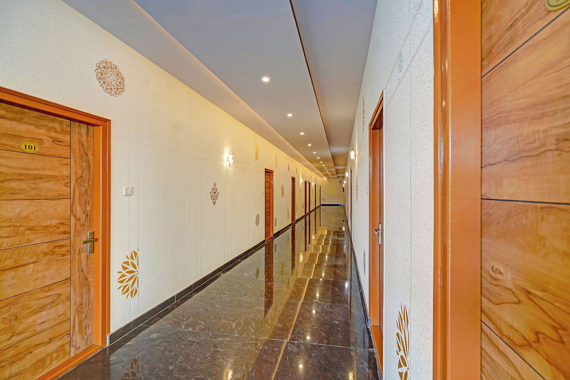 A hotel corridor with wooden doors, numbered room signs, and decorative wall patterns.