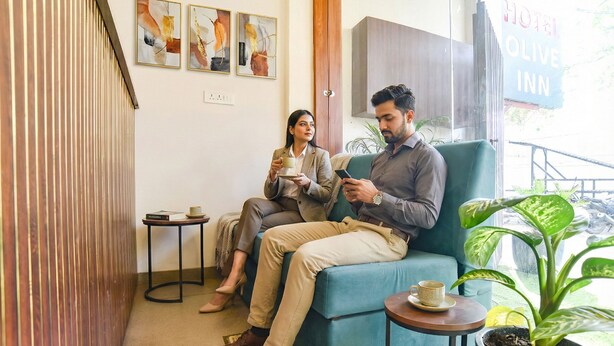 A room with a blue sofa, a small table with a cup, and a potted plant. There are abstract paintings on the wall and a sign for the hotel. - Fabhotel Olive Inn (Indore)