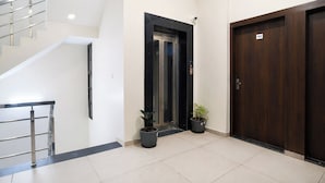 A modern hotel lobby with a staircase, a black-framed elevator, and a wooden door marked with the number 101. - Fabhotel Olive Inn (Indore)