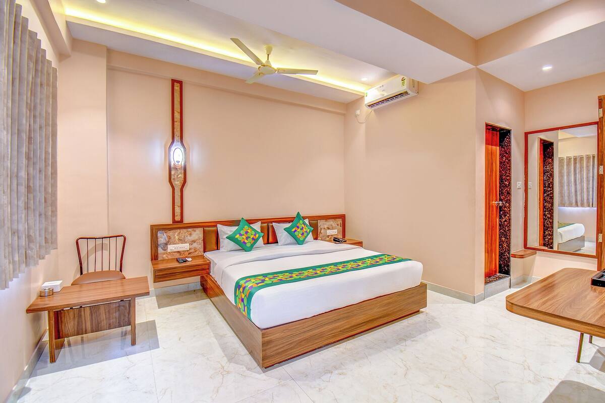 A hotel room with a wooden bed, a nightstand, a desk, a chair, a ceiling fan, and a mirror.