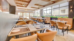 Een modern restaurant met hoge plafonds, grote ramen en diverse zitmogelijkheden, zoals tafels en zithoeken.