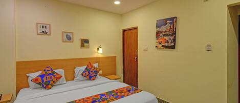A hotel room with a bed, a wooden headboard, a wall-mounted lamp, and a door.