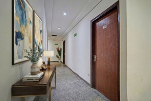 A hallway with a wooden door labeled "G-1", a desk with a vase and books, and framed abstract art on the wall. - Fabhotel Pingla Residency (New Delhi)