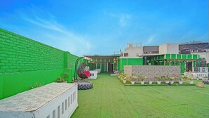 A courtyard with artificial grass, a hanging chair, potted plants, and a white bench. - Fabhotel Pingla Residency (New Delhi)