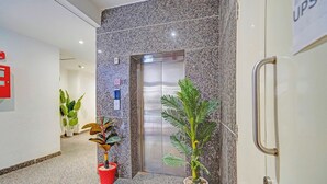 An elevator with a granite wall, a red fire alarm, and two potted plants. - Fabhotel Pingla Residency (New Delhi)